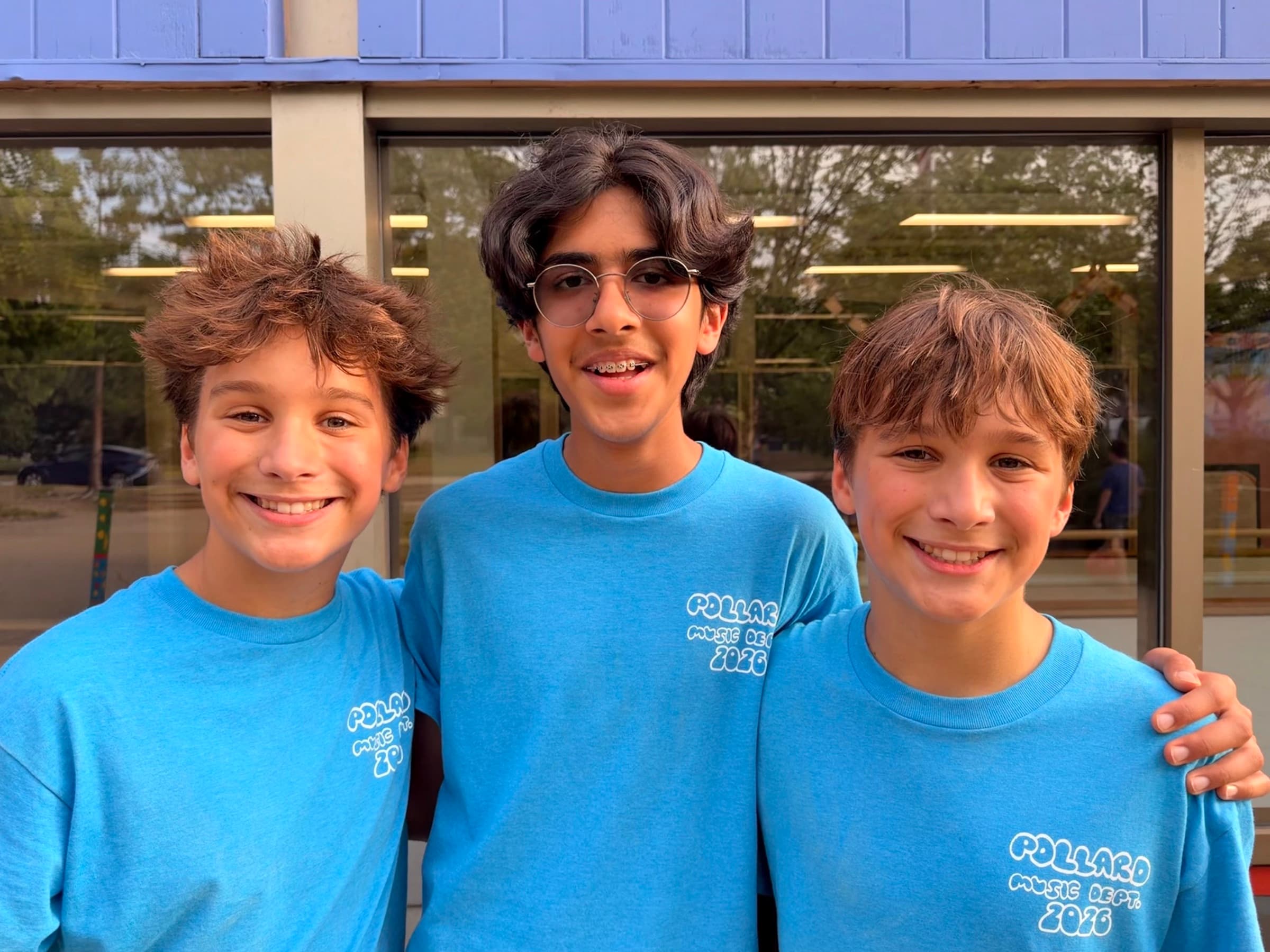 Three Pollard music-department students in matching blue shirts smiling together outside the school.